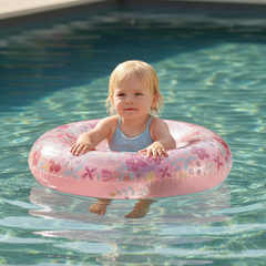 Kleinkind sitzt mit einem rosa Kinder-Schwimmring im Blumen-Design im Pool und genießt einen sonnigen Sommertag. Der aufblasbare Schwimmring eignet sich ideal für Pool, Garten und Urlaub.